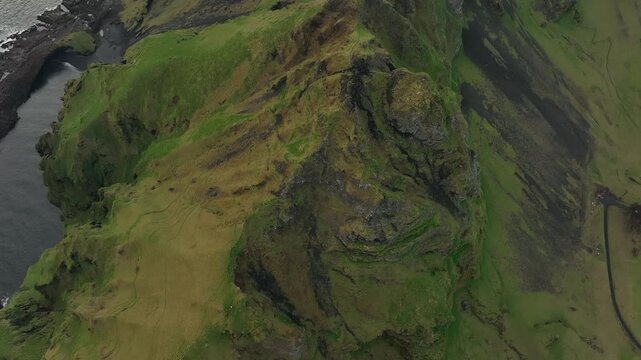 Aerial view of the lush green cliffs and rugged coastline of the Westman Islands, Iceland, featuring dramatic rock formations and a secluded ocean inlet.