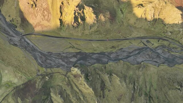 An aerial view of Thakgil, Iceland, showcasing a winding road crossing a braided river amidst dramatic volcanic terrain and mossy cliffs.