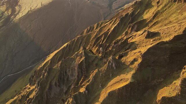 Aerial view of rugged slopes in Thakgil, Iceland, bathed in golden sunlight, highlighting sharp ridges and dramatic terrain.