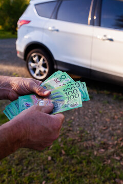 Middle aged mans hand holding one hundred dollar notes in Australian cash to pay for car