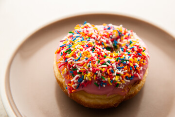 a doughnut covered with pink icing and rainbow sprinkles on a plate