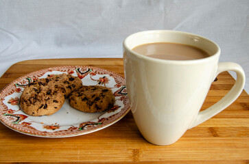 Chocolate chip cookies on a plate and a mug of coffee with a wooden background