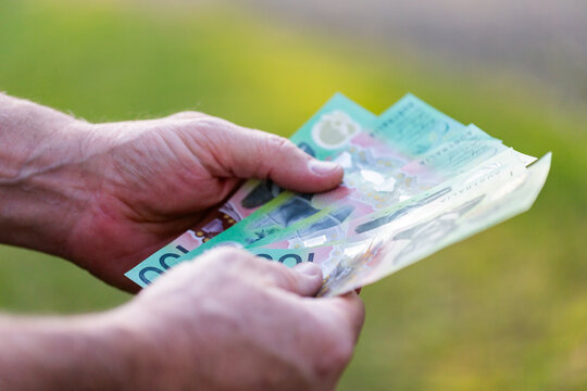 Middle aged man&rsquo;s hand holding hundreds of dollars of Australian cash