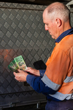 Middle aged man holding hundreds of dollars of Australian cash beside meal tool box on ute