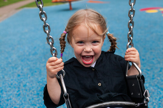 Happy little girl laughing and swinging on swing at park on overcast day