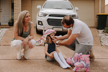 Dad helping daughter fix her helmet while mum sits on the side..