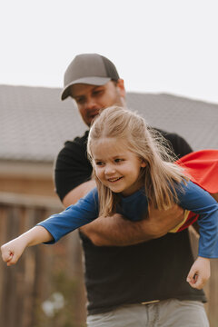 Dad simulating a flight for daughter in superhero costume.