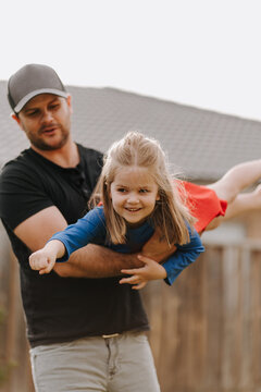 Dad simulating a flight for daughter in superhero costume.