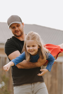 Dad simulating a flight for daughter in superhero costume.