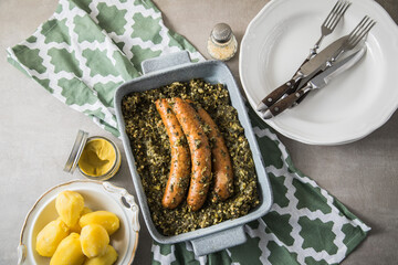 Oldenburger Grünkohl mit Pinkel Kohlwurst in Schale, Salzkartoffeln und Senf auf gedeckten grau Tisch mit grün Tuch, Teller, Besteck rustikal 