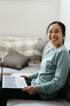 Happy woman sitting on the couch while holding her laptop.