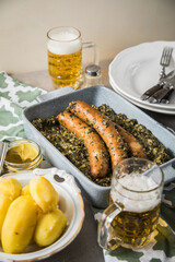 Oldenburger Grünkohl mit Pinkel Kohlwurst in Schale, Salzkartoffeln, Senf und Bier auf gedeckten grau Tisch mit grün Tuch, Teller, Besteck rustikal 
