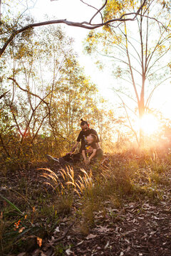 Aboriginal Worimi dad with muscular dystrophy and young son sitting together in bushland at sunset