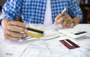 Asian man sitting at desk holding credit card calculate receipt, expenses and all loan bills that...