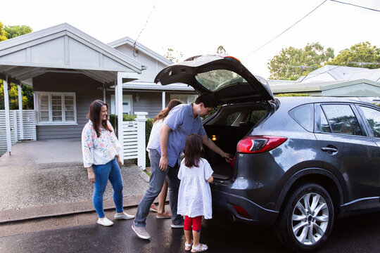 Two young girls helping dad get things loaded into boot of family car