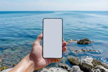 Man holding phone by sea with blank screen.
