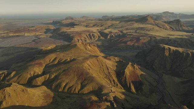 An expansive aerial view of Thakgil, Iceland, highlighting vast volcanic ridges, winding valleys, and dynamic textures under golden sunlight.
