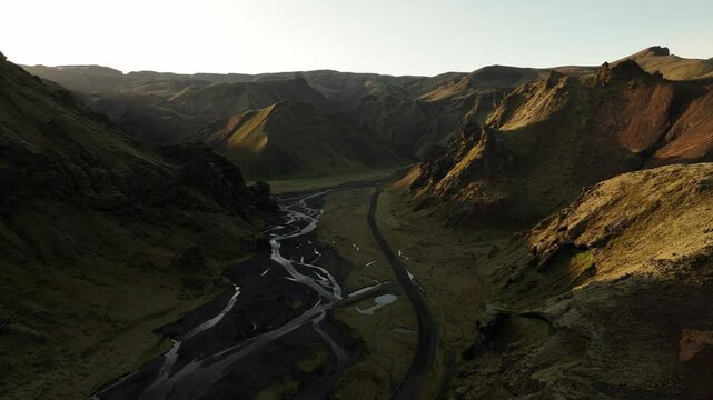 A breathtaking aerial view of Thakgil, Iceland, showcasing rugged volcanic cliffs, winding streams, and golden sunlight across the valley.