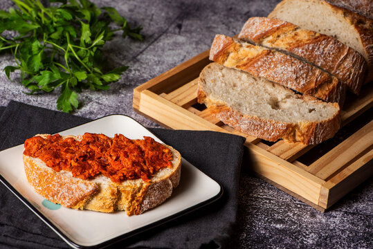 Slice of bread with sobrasada spread, next to several slices of bread on a cutting board, close-up.