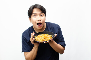 ecstatic and surprised young Asian man holding a plate of fried instant noodles.