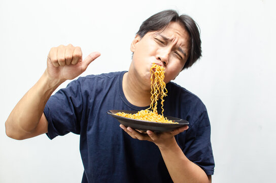 young asian man enjoying and swallowing fried noodles with mouth full of noodles.