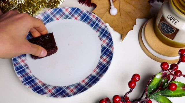 An unrecognizable girl is taking three pieces of quince cheese off of a plate placed in a christmasy background.