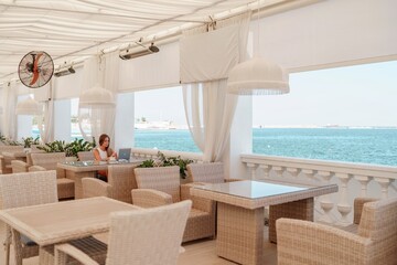 Woman coffee cafe laptop sea. Female freelancer using laptop on coffee break in modern cafe with sea view in the morning