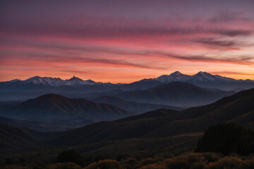 Obraz premium Mountain layers in silhouette, nearest dark, farthest fading; golden-pink sunrise, thin clouds reflecting warm light, serene and captivating
