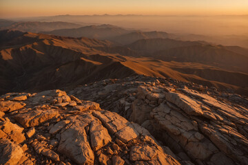Rugged brown-golden mountains under a golden sunset sky; orange gradient above, stones below softly glowing with warm, peaceful light