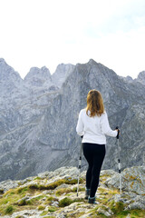 Naklejka premium A girl in sportswear stands leaning on hiking boards at the top and enjoys the view of the mountains. Walking the trail between Volusnica and Talijanka peaks in Prokletije National Park, Montenegro.