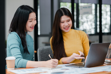 Two women working together in an office, discussing ideas and using a laptop, showcasing teamwork and collaboration.