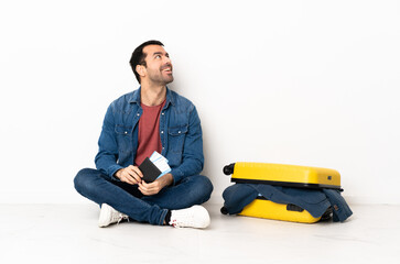 Caucasian handsome man with a suitcase full of clothes sitting on the floor at indoors thinking an...
