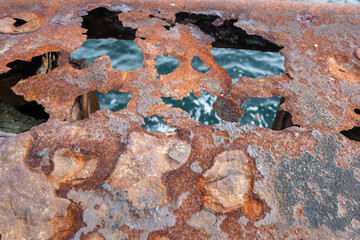 Altes, vom Rost zerfressenes Metall. Durch die Löcher ist schon das Wasser zu sehen. Ein...