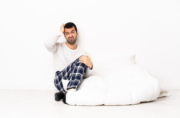 Caucasian man in pajamas sitting on the floor at indoors with an expression of frustration and not...