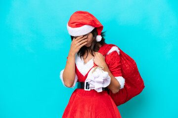 Young hispanic woman dressed as mama noel holding a sack isolated on blue background with tired and sick expression
