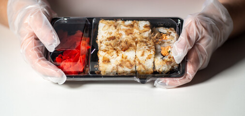 Sushi to go concept. Take away box with sushi rolls in woman hands in gloves. Food delivery concept. Take away food concept.
