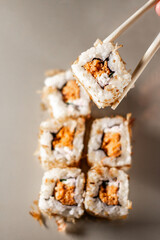 Chopsticks taking portion of sushi roll. Sushi rolls with salmon cream cheese and cucumber. Isolated. Sushi roll on grey background.