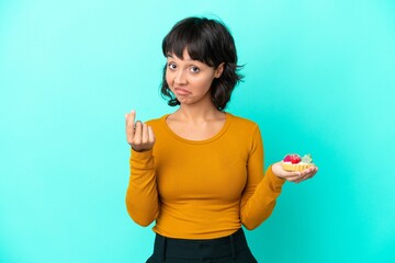 Young mixed race woman holding a tartlet isolated on blue background making money gesture