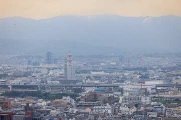 Naklejka premium A serene view of Kyoto’s urban expanse framed by distant mountains under a soft, hazy sky. 