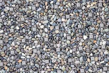 A detailed close-up view of gray and multicolored gravel interspersed with metallic anchors embedded into the ground. This textured composition captures an intriguing mix of natural stones.