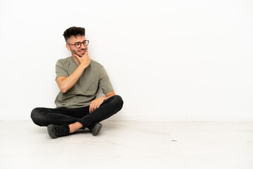 Young caucasian man sitting on the floor isolated on white background looking to the side