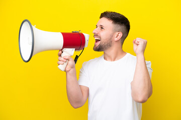 Young caucasian man isolated on yellow background shouting through a megaphone to announce something in lateral position