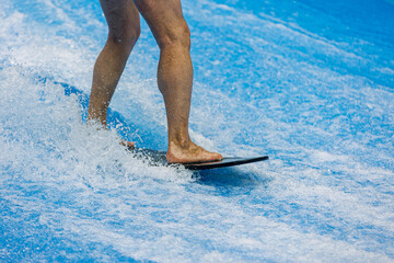 A man rides a surfboard on a wave simulator indoors. Young surfer during training on generated...