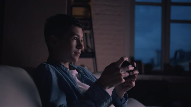 Nighttime Gaming: Boy on the Couch at Home, Engrossed and Expressing Emotion While Playing Video Games