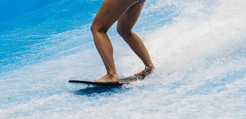 A man rides a surfboard on a wave simulator indoors. Young surfer during training on generated waves. Water sports and recreation.