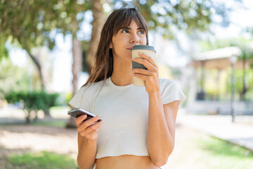 Young woman at outdoors using mobile phone and holding a coffee