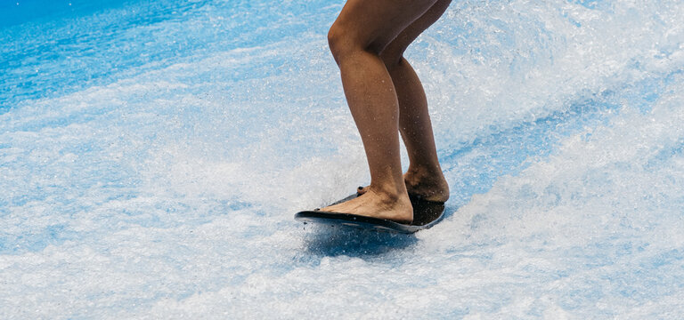 A man rides a surfboard on a wave simulator indoors. Young surfer during training on generated waves. Water sports and recreation.