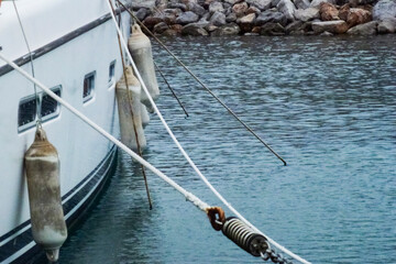 A part of an old white yacht, sea mooring ropes in a marina on the background of water, stones. Close-up.