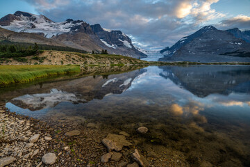 Naklejka premium The panoramic view of snowy mountain and colorful clouds with lake reflections at ice field center of Jasper National Park. Famous Athabasca glacier in Canada.