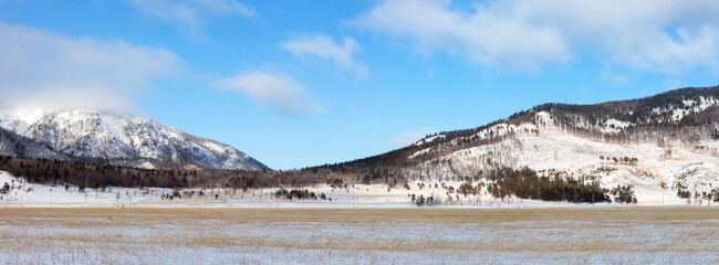 Panoramic view of Goloustnaya River valley framed by snow-capped mountains on sunny January day....